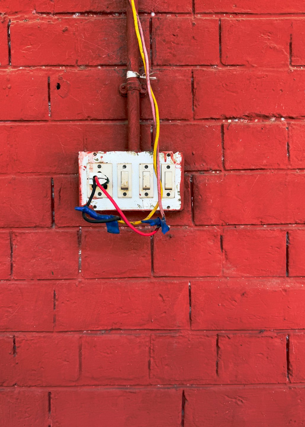 Alter Elektroschaltkasten an einer roten Ziegelwand mit bunten Kabeln.