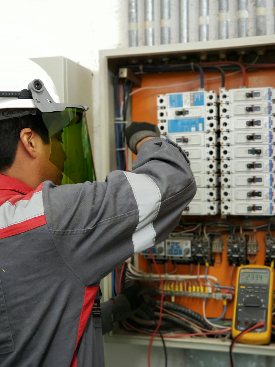 Techniker inspiziert offenen Elektroschaltkasten mit Sicherungen und Verkabelung.