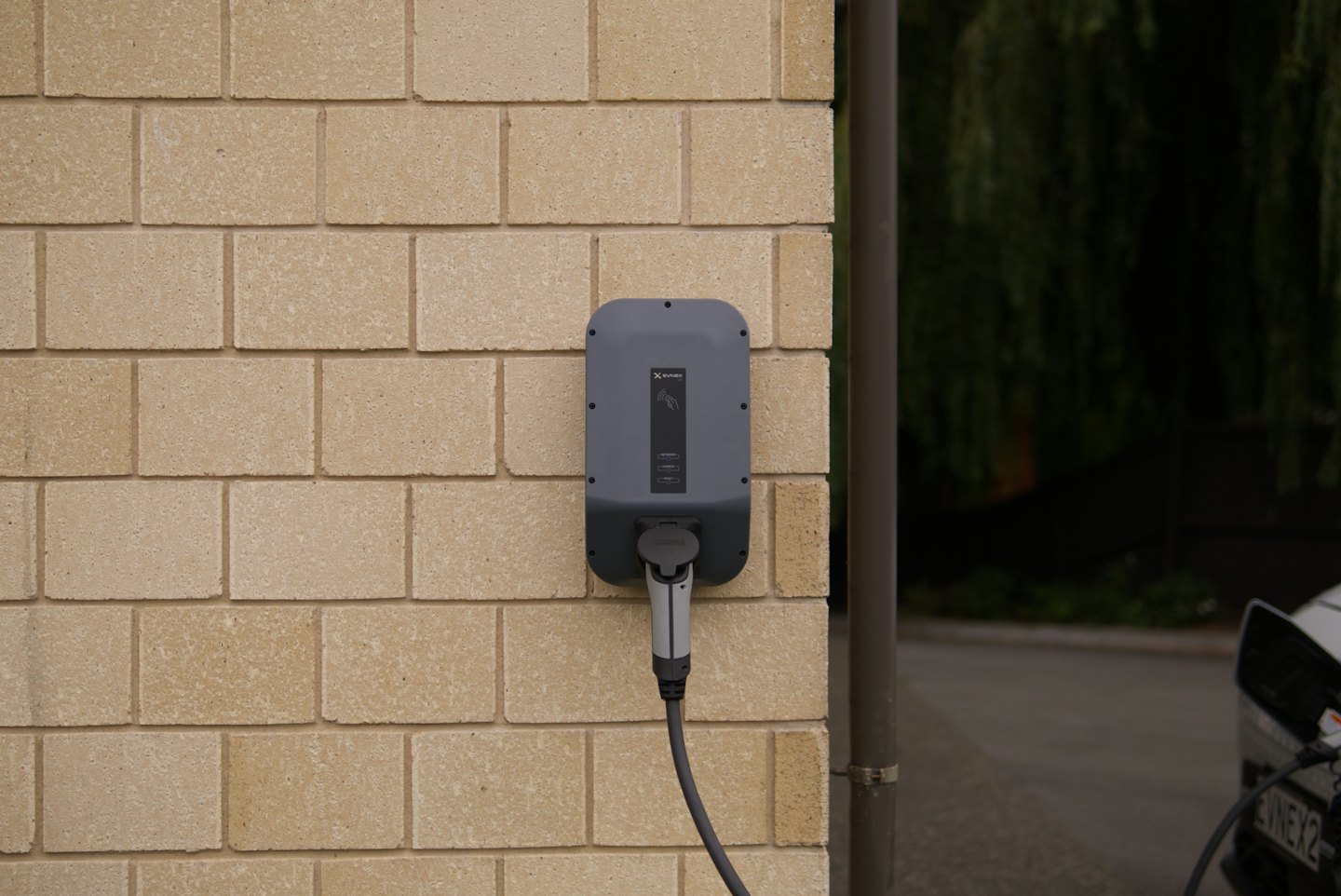 Ladegerät für Elektroautos, das in ein weißes Auto an einer Ziegelwand gesteckt ist.